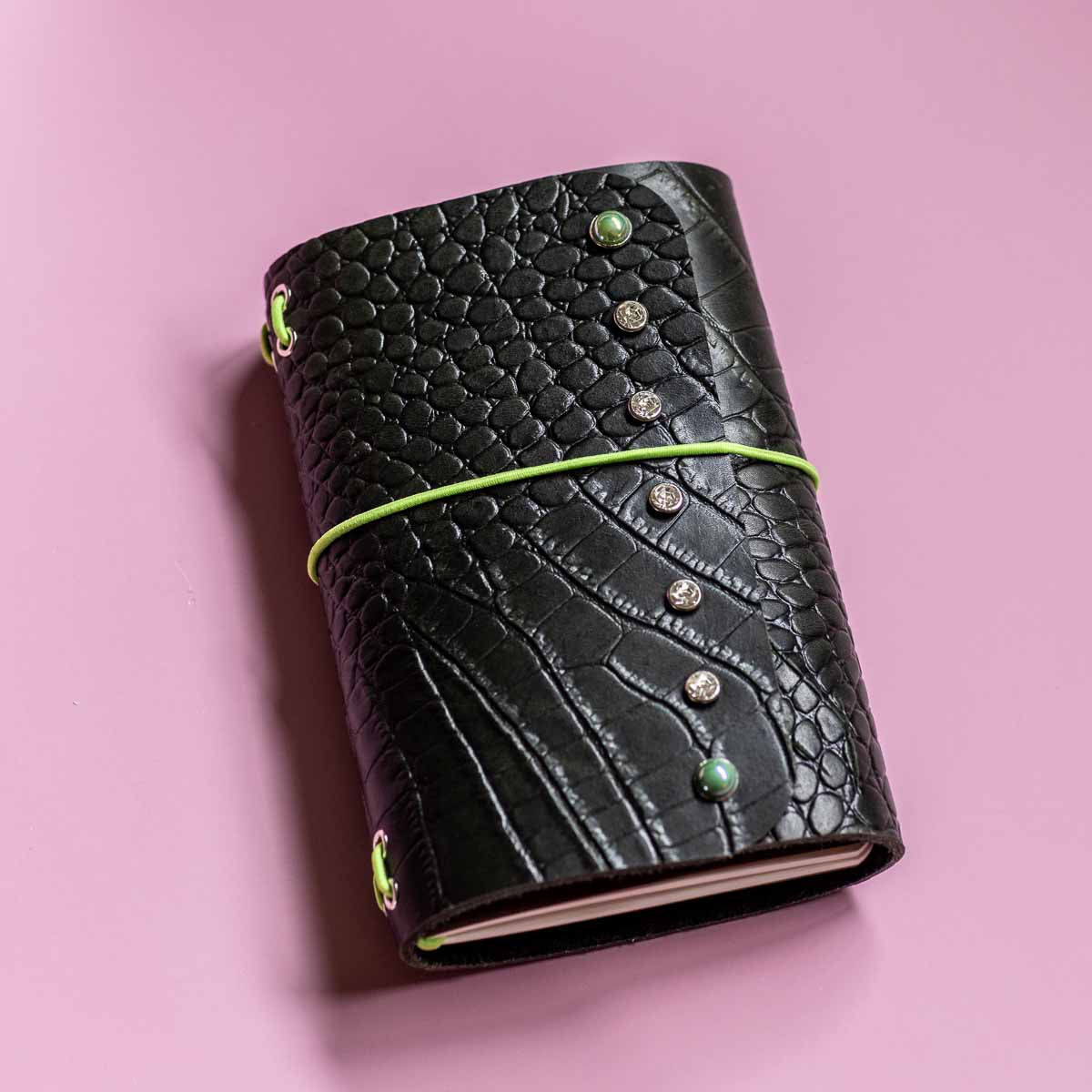 Black textured leather notebook with decorative elements on a pink background