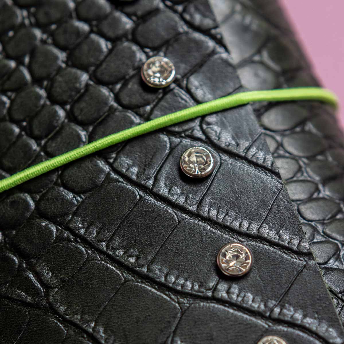 Close-up of a black textured surface with green thread and metallic buttons.