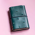 Green leather notebook with decorative studs on a pink background