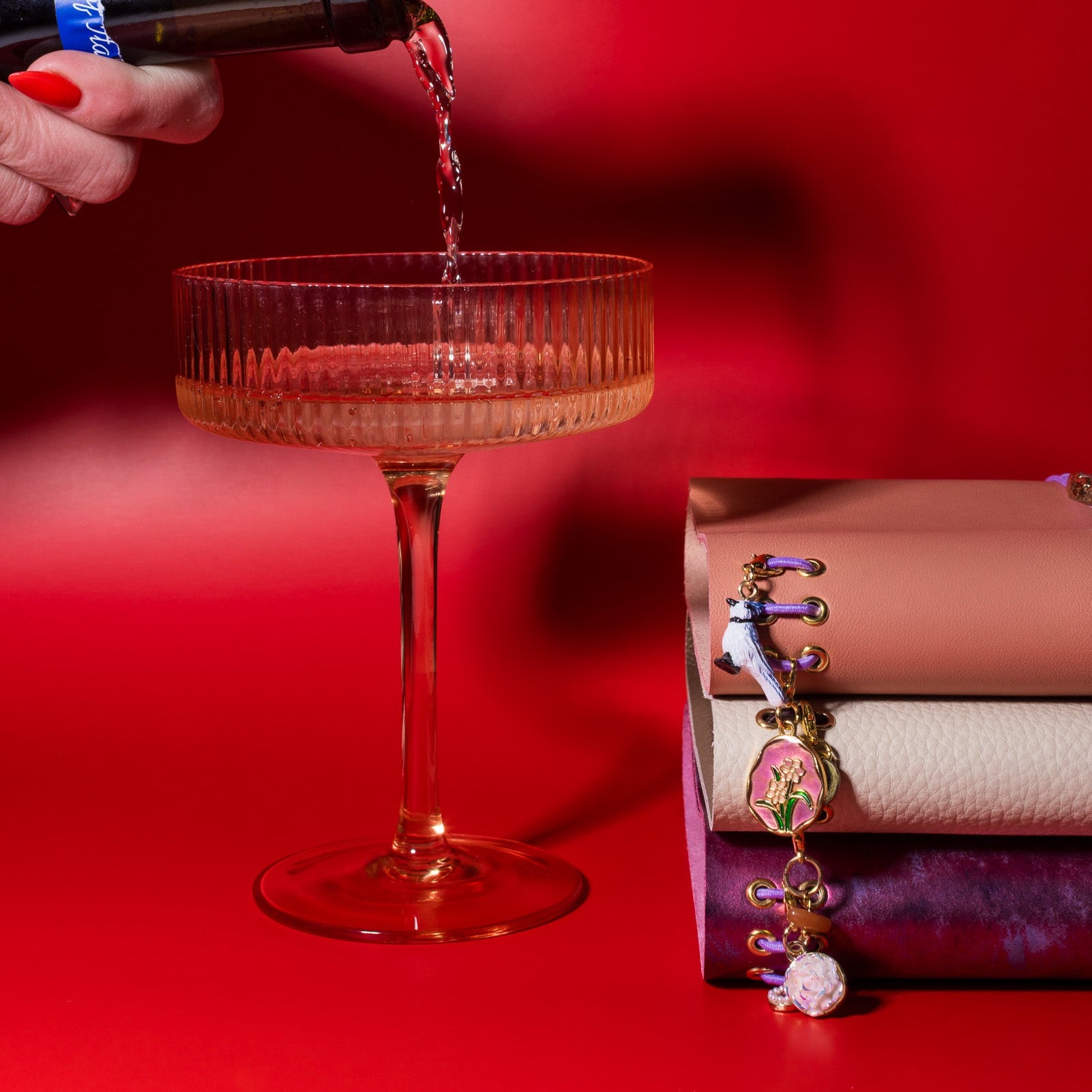 Hand pouring red wine into a glass with a red background