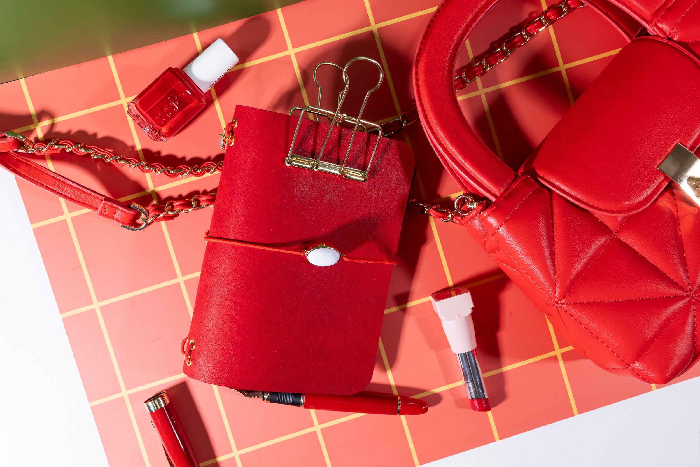 Red handbag, nail polish, and other accessories on a red checkered surface